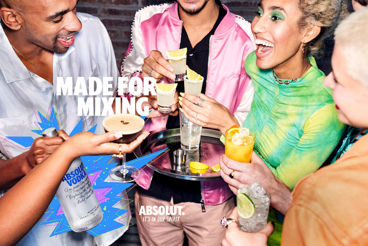 Group of diverse adults mixing cocktails with Absolut vodka in an indoor setting, drinks displayed on a silver tray, smiling and festive.
