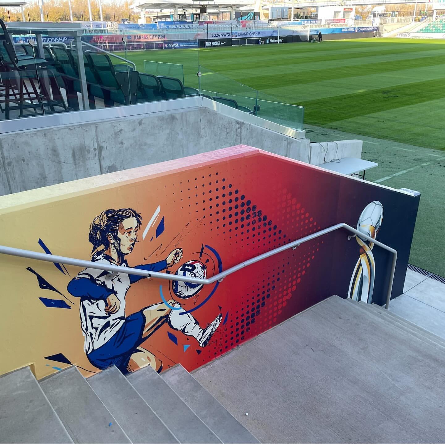 Illustration on wall of a soccer player kicking a soccer ball near stairs and a soccer field on a sunny day at the stadium.
