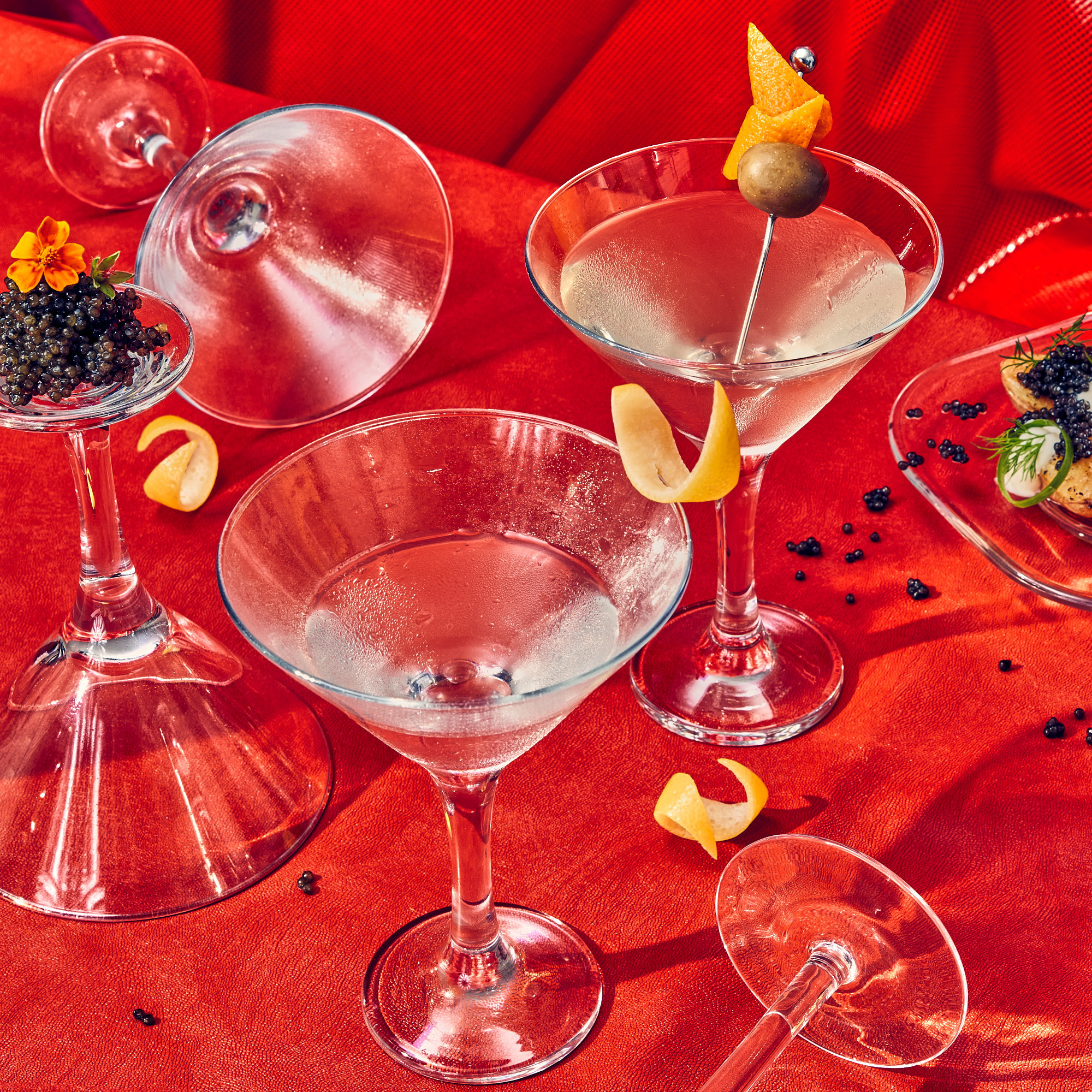 Multiple martini glasses with some filled with martinis and caviar on a red surface, suggesting a luxurious cocktail party setting.