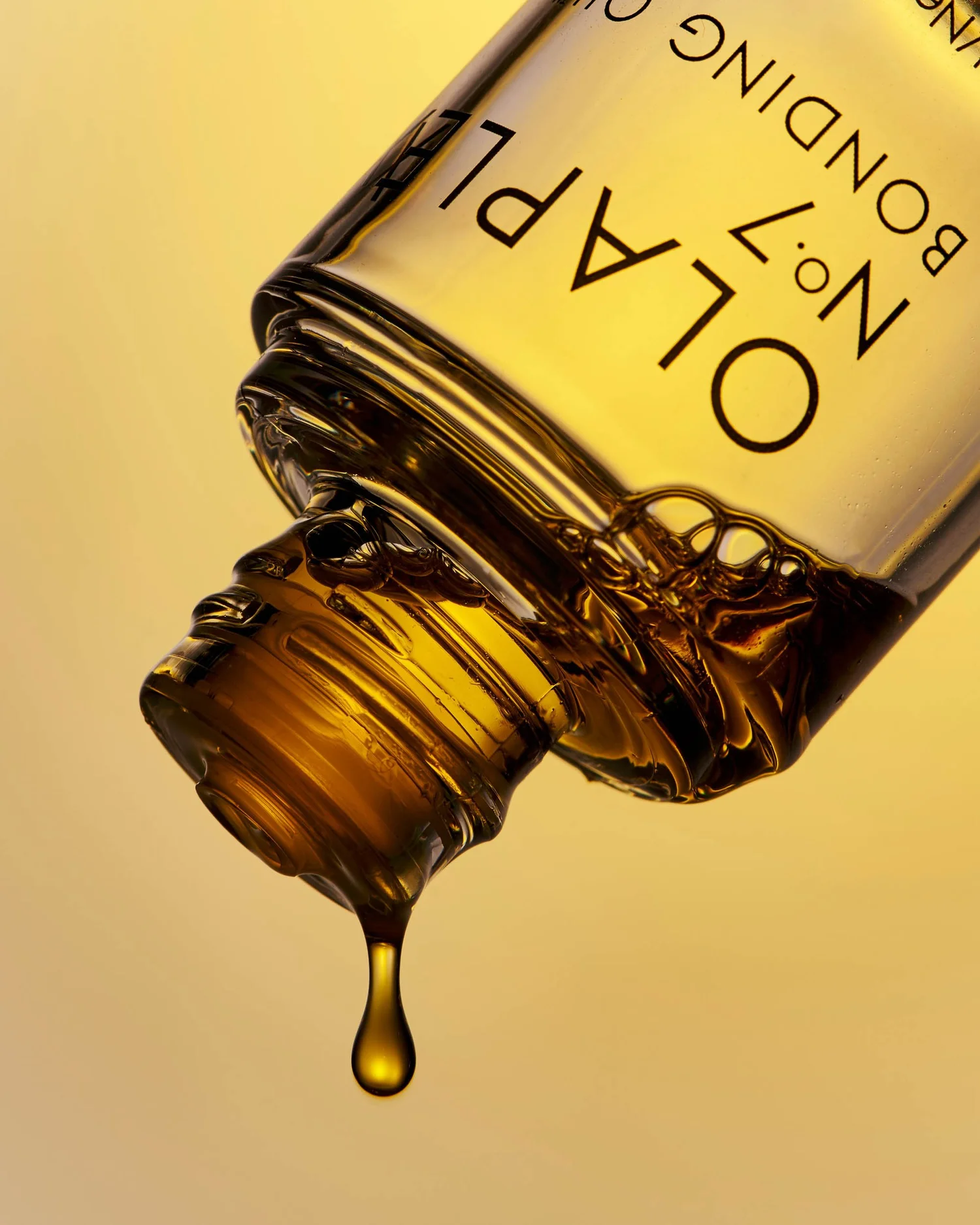 Close-up shot of a bottle of Olaplex No. 7 Bonding Oil with a single drop of oil suspended from the bottle's open top.