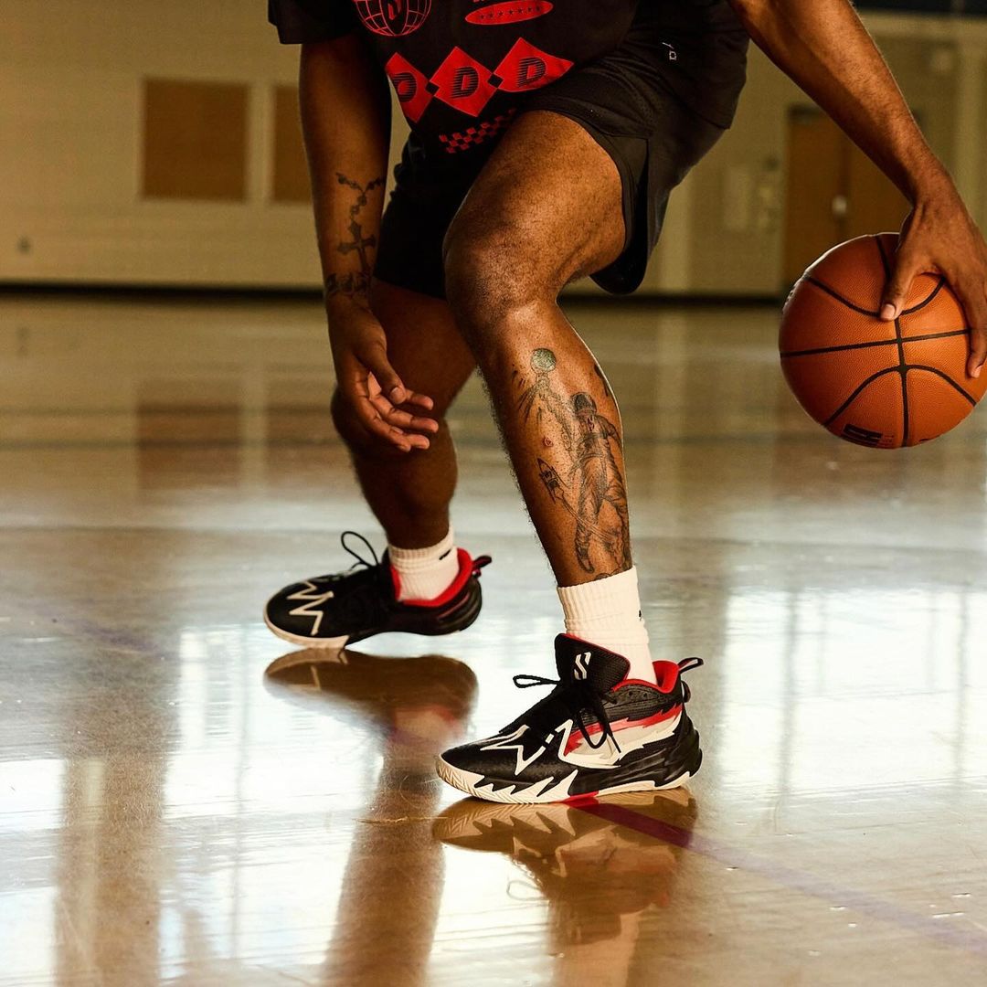 Basketball player dribbles indoors on a glossy hardwood court; tattoos on the legs and arms are also in focus.
