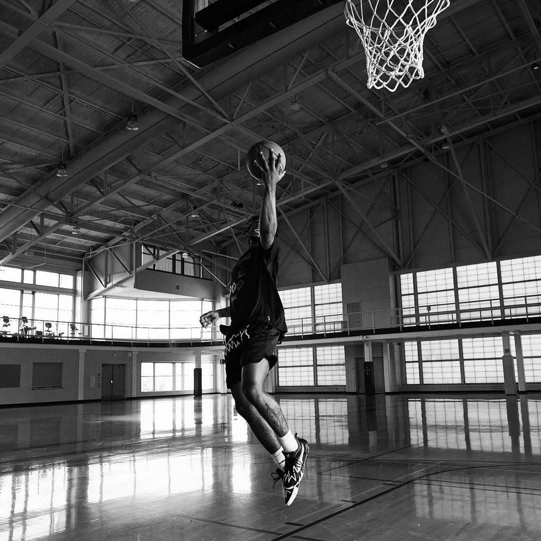 Monochromatic action shot: An adult male basketball player leaps mid-air towards the net with the ball in hand inside a gymnasium.