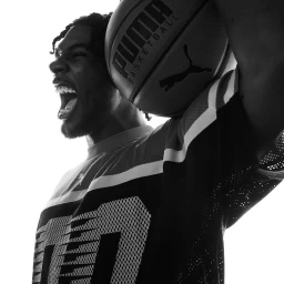 Black and white portrait of a black man wearing a mesh jersey holding a Puma basketball near his shoulder.