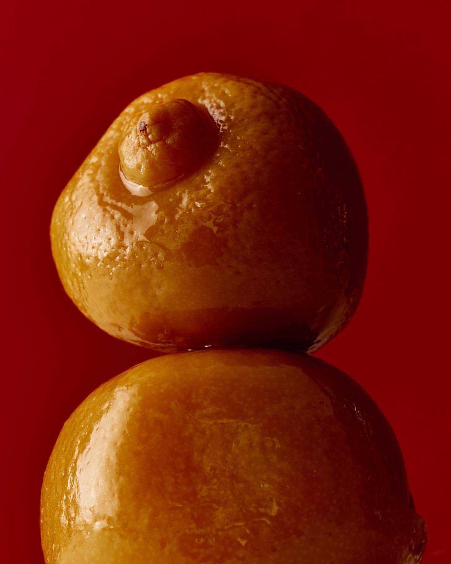 Close-up studio shot of two stacked oranges against a plain red backdrop, emphasizing the fruit's textures and unique forms.
