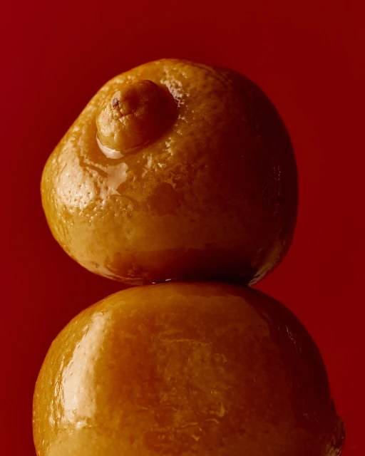 Close-up studio shot of two stacked oranges against a plain red backdrop, emphasizing the fruit's textures and unique forms.
