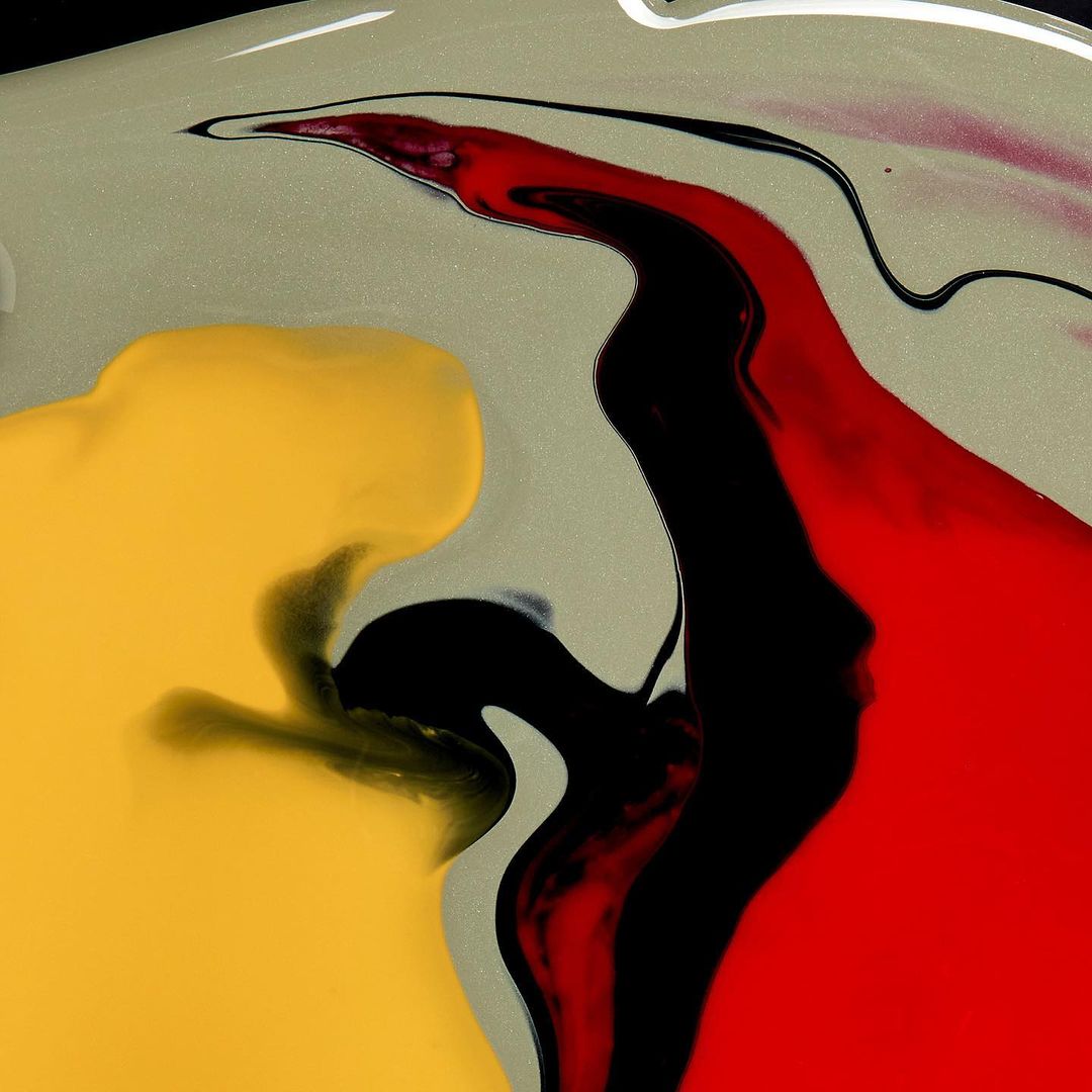 Abstract fluid art featuring dynamic streaks of yellow, black, red, and grey, creating a visually striking and modern design.