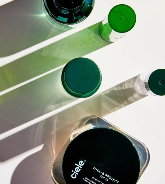 Overhead shot of Ciele cosmetics containers and bottles in varying sizes, with light and shadow play on a solid white surface.