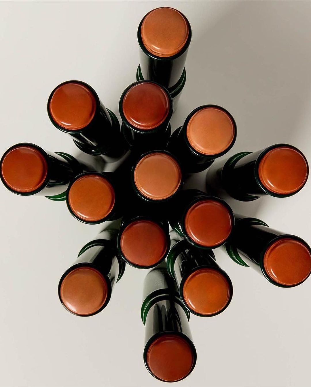 Overhead shot of a collection of black-tubed bronze, brown, and tan makeup sticks arranged on a white surface, emphasizing the color variation.