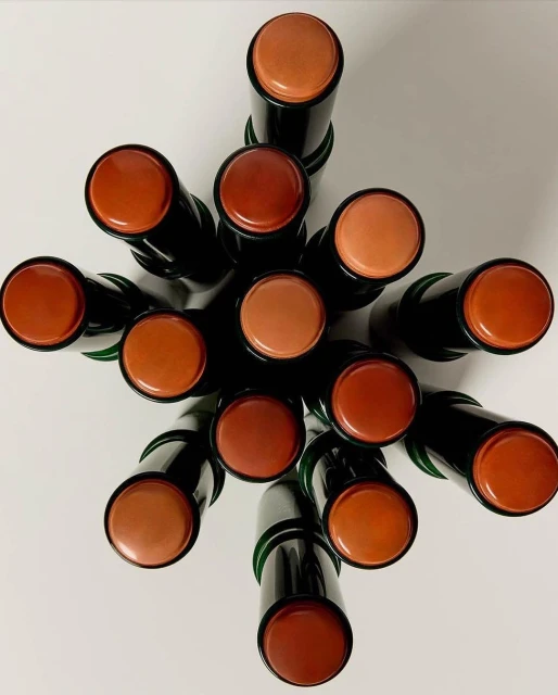 Overhead shot of a collection of black-tubed bronze, brown, and tan makeup sticks arranged on a white surface, emphasizing the color variation.