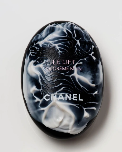 Close-up of Chanel Le Lift La Crème Main hand cream in an egg-shaped black case with white cream accents on a white background.