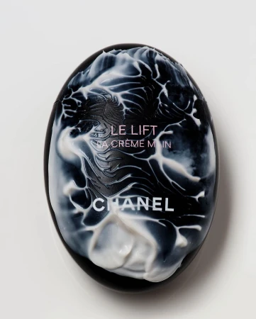 Close-up of Chanel Le Lift La Crème Main hand cream in an egg-shaped black case with white cream accents on a white background.