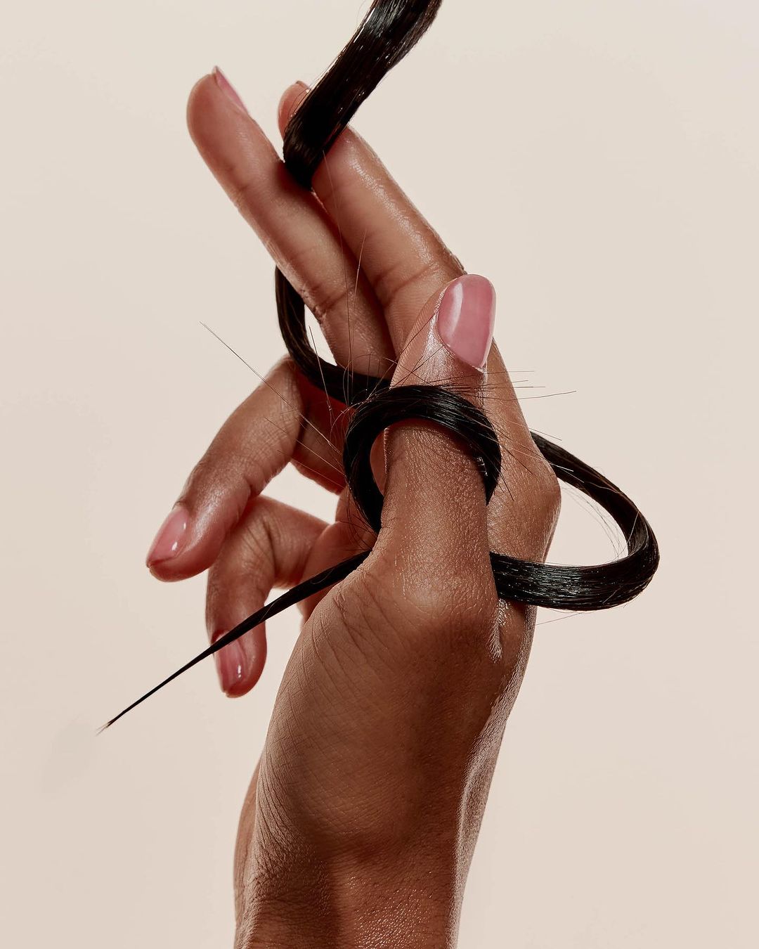 Close-up shot of a hand holding a strand of dark hair, set against a soft, neutral background. The focus is on the texture of the hair.