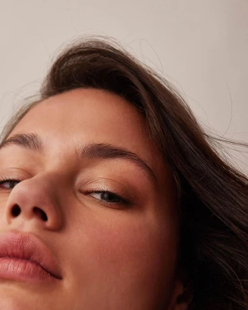 Close up low angle portrait of a woman with dark hair looking down at the camera against a neutral background