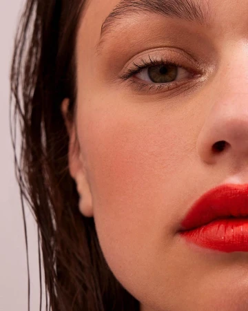 Close-up beauty portrait of a woman with wet hair, natural makeup, and vibrant red lipstick.