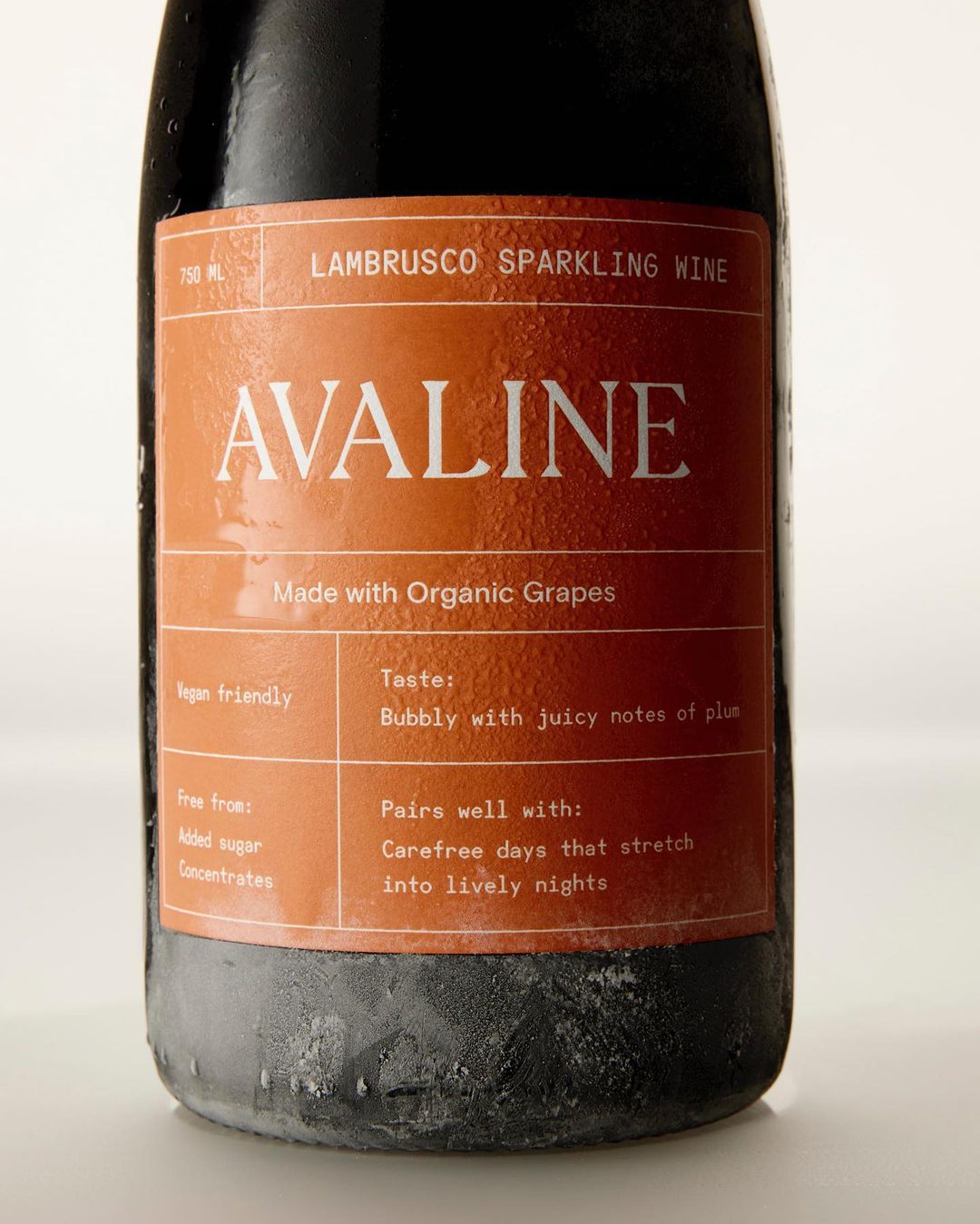 Icy bottle of Avaline Lambrusco sparkling wine with a brown label detailing the wine's organic grapes, vegan-friendly nature, and taste notes.