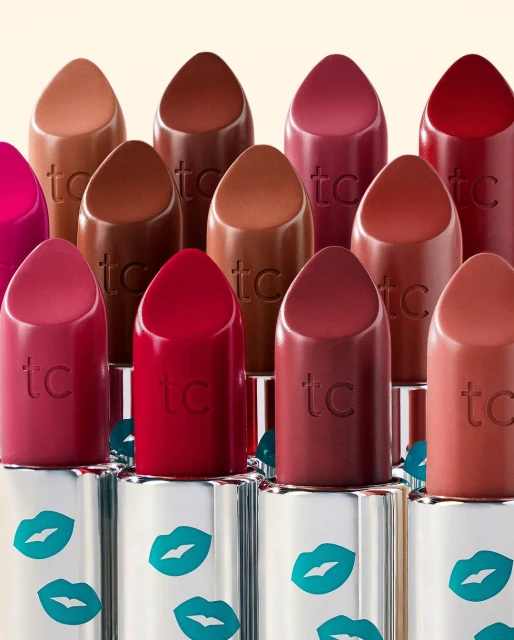 Close-up of assorted lipsticks in varying shades, arranged in rows with silver tubes adorned with teal lip designs, beauty product.