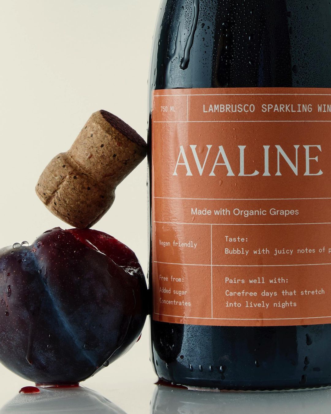 Close-up shot of a bottle of Avaline Lambrusco sparkling wine with a cork and a plum, showcasing the product's natural ingredients.