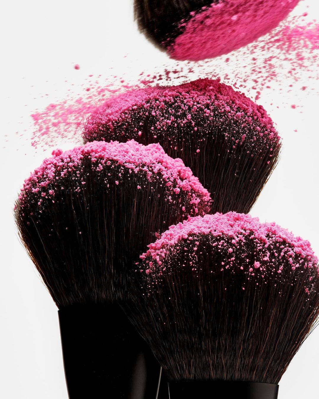 Close-up of several makeup brushes coated with bright pink powder against a white backdrop, creating a striking visual for beauty concepts.
