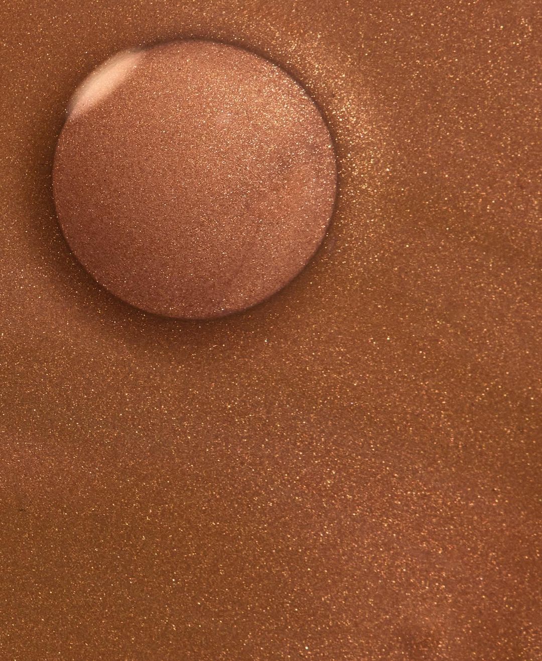 Close-up of a shimmery copper-toned bronzer compact with a smooth, reflective surface showing warm, metallic shades and textures.