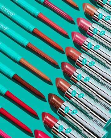 Overhead shot of multiple colorful lipsticks and lip liners in a diagonal pattern on a turquoise background for beauty and cosmetics.