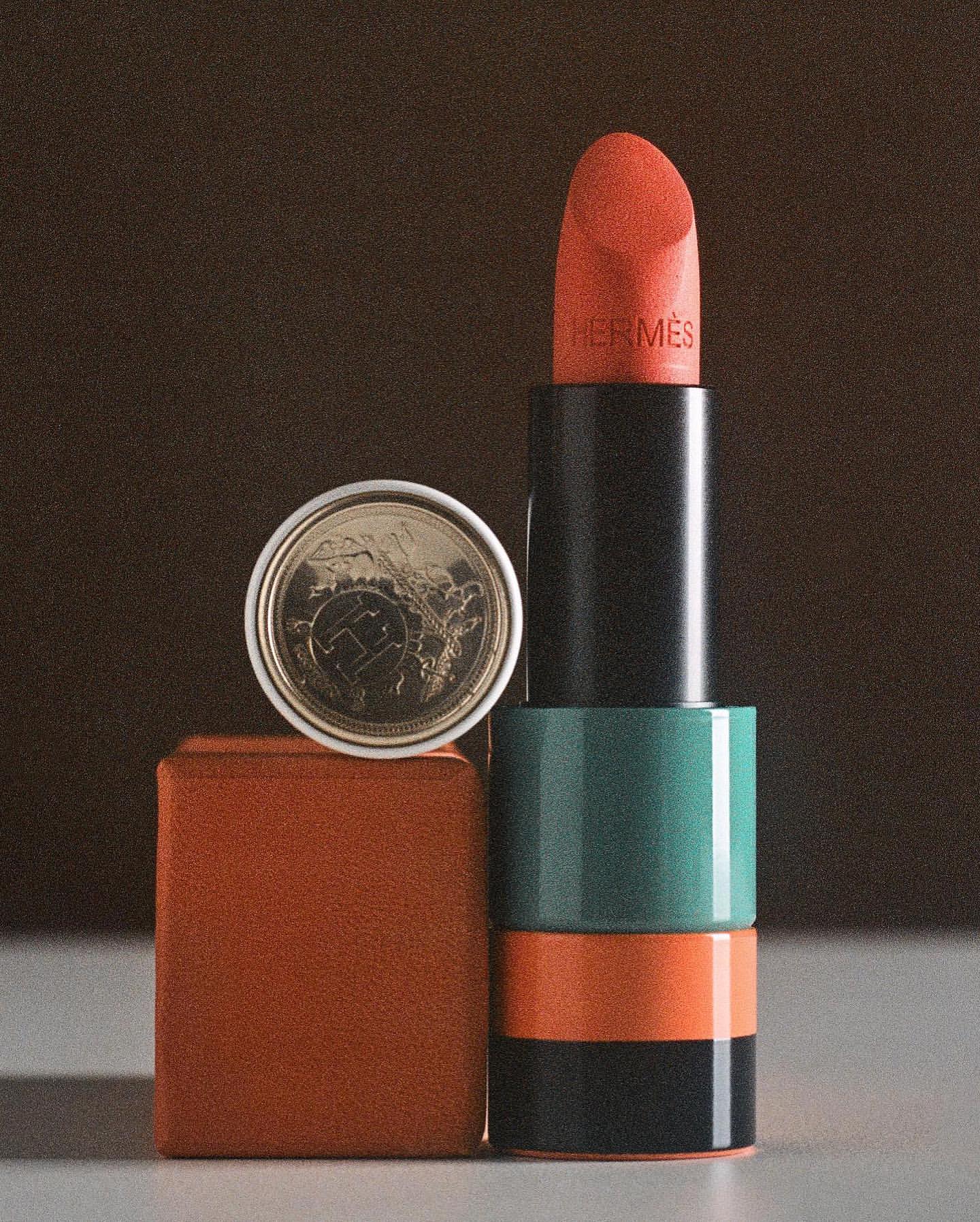 Still life shot of Hermès lipstick in red orange beside a euro cent coin on a brown cube against a blurred brown background.