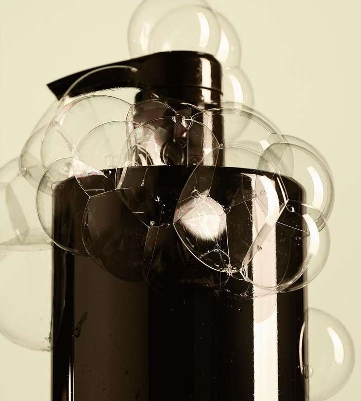 Close-up studio shot of a black pump bottle surrounded by clear soap bubbles against a light yellow background, creating a clean and fresh aesthetic.