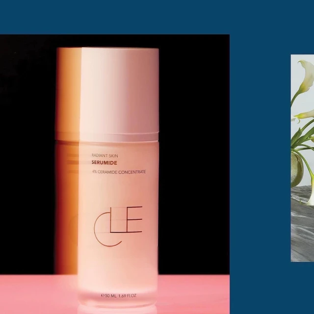 Close-up studio shot of a frosted pink CLE serum bottle on a pink surface against a dark background, next to white Calla lilies.