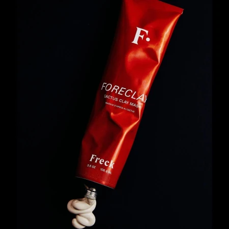 Studio shot of 'Foreclay' cactus clay mask tube from Freck Beauty, with its pale contents spilling out against a black background.