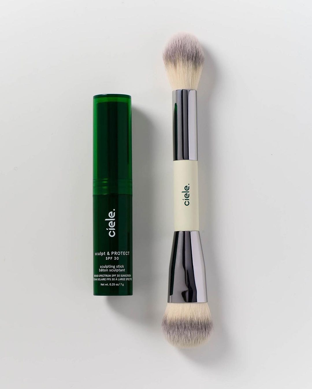 Ciele cosmetics product shot featuring a green sculpting stick and a double-ended makeup brush against a neutral background.
