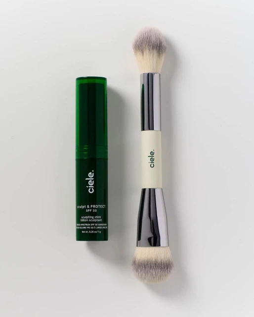 Ciele cosmetics product shot featuring a green sculpting stick and a double-ended makeup brush against a neutral background.