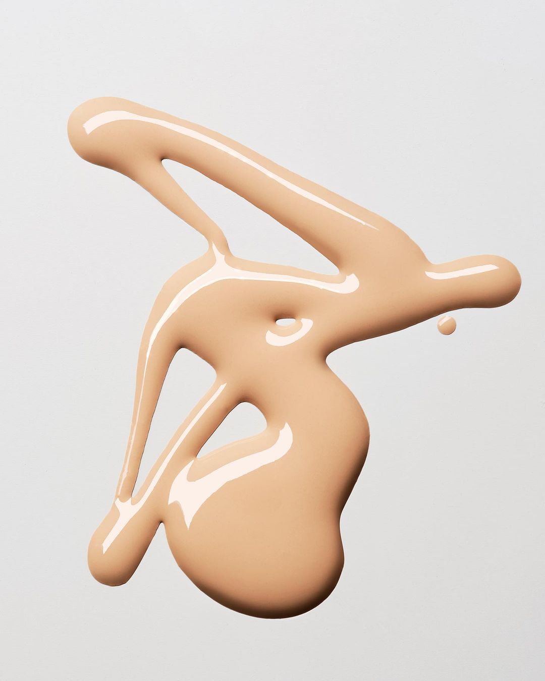 Close-up of beige foundation makeup swatch with glossy finish, against a clean, neutral background for beauty product showcase.