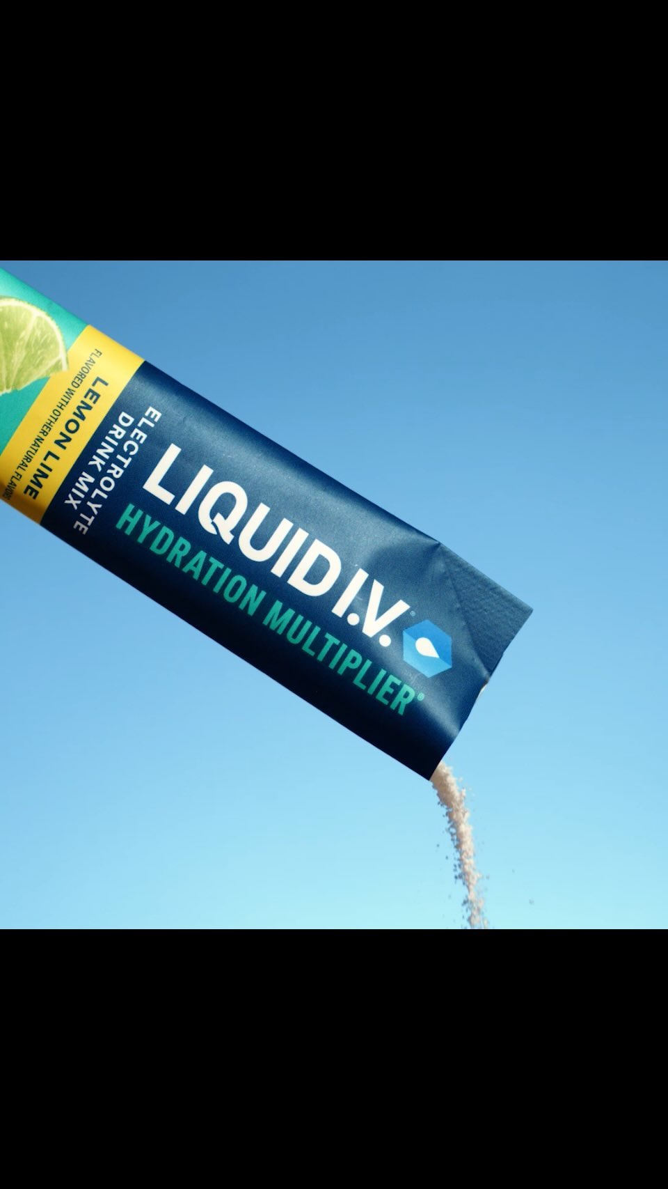 A single-use packet of Liquid I.V. electrolyte drink mix being poured against a clear blue sky background in a studio shot.