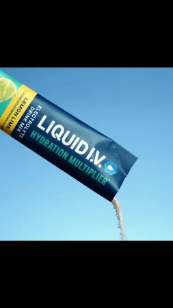 A single-use packet of Liquid I.V. electrolyte drink mix being poured against a clear blue sky background in a studio shot.