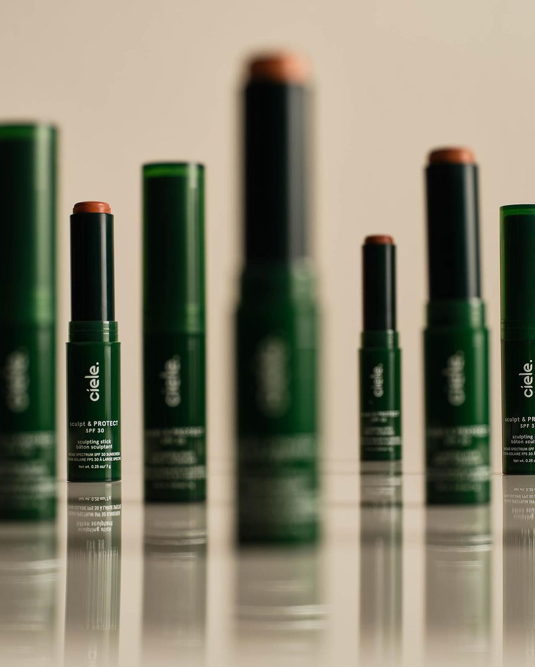 Several cie le Conceal + Protect SPF 30 makeup sticks and tubes, in dark green packaging, lined up on a reflective surface.