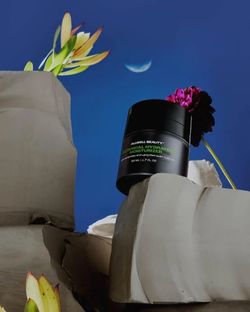 Cosmetic product shot: black jar of moisturizer with flowers and stone fragments against a blue gradient background with a moon.