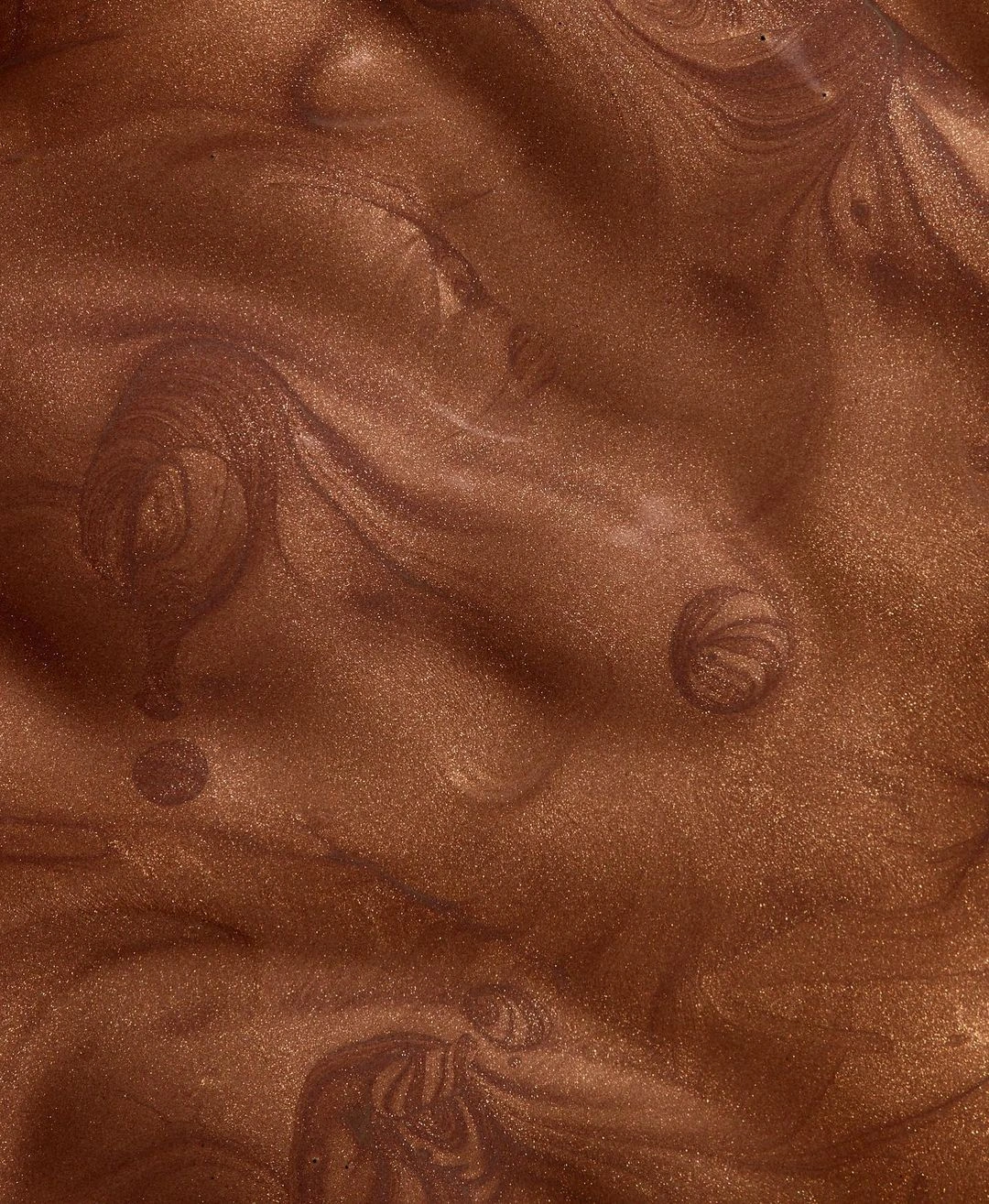 Macro close-up shot of shimmering metallic bronze cosmetic liquid texture with swirls.