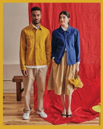 Man in yellow jacket and woman in blue jacket standing before a red backdrop, photographed by Bryan Derballa