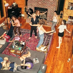 High-angle view of a group of friends partying and dancing in a rustic living room with wooden walls and a large brick fireplace.