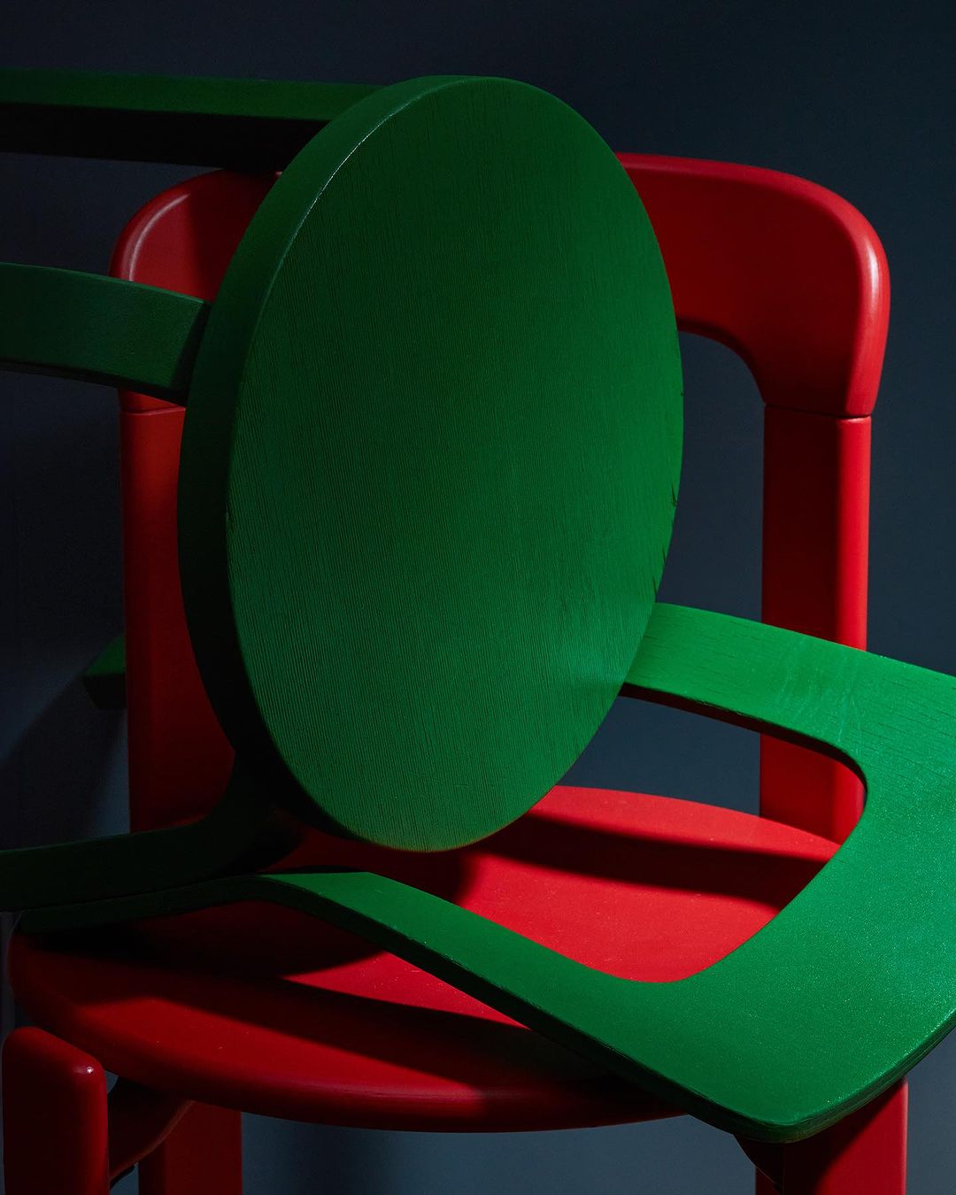 A vibrant, abstract composition featuring a red chair partially obscured by a deconstructed green chair, set against a dark background.