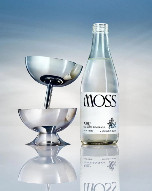 Elegant still life showcases a sleek metal cocktail tower beside a bottled beverage against a graduated blue backdrop with reflective surface.