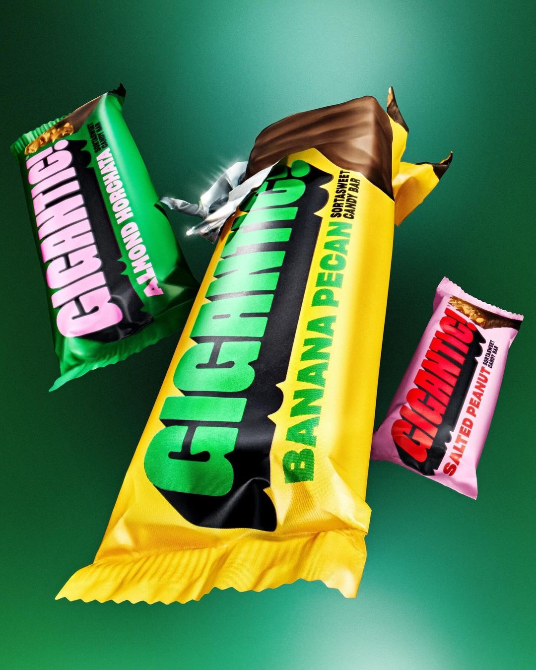 Three Gigantic! candy bars with different flavors arranged on a green background. The candy bar wrappers are colorful and glossy.