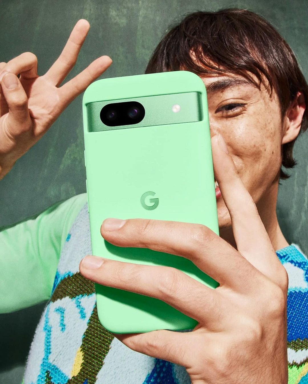 Smiling man holds a light green Google Pixel phone in its matching protective case, displaying the camera.