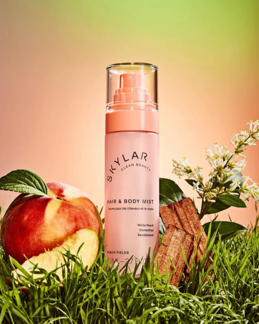 Skylar Clean Beauty hair and body mist bottle alongside a sliced peach, greenery, and floral accents against a gradient backdrop.