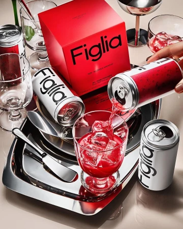 Pouring a red Figlia non-alcoholic aperitivo drink from a white and red can into a stemmed glass with ice on a silver tray.