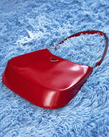 Shiny red Prada Cleo handbag displayed on a soft, light blue faux fur background. Fashion product photography with a luxury aesthetic.