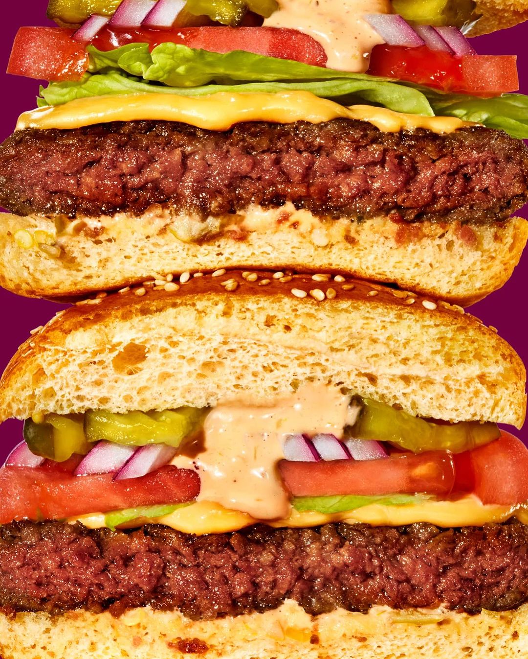 Stacked veggie burgers close-up on a purple background. Sesame seed buns, meatless patties, lettuce, tomato, onion and special sauce.