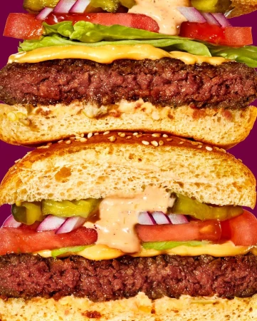 Stacked veggie burgers close-up on a purple background. Sesame seed buns, meatless patties, lettuce, tomato, onion and special sauce.