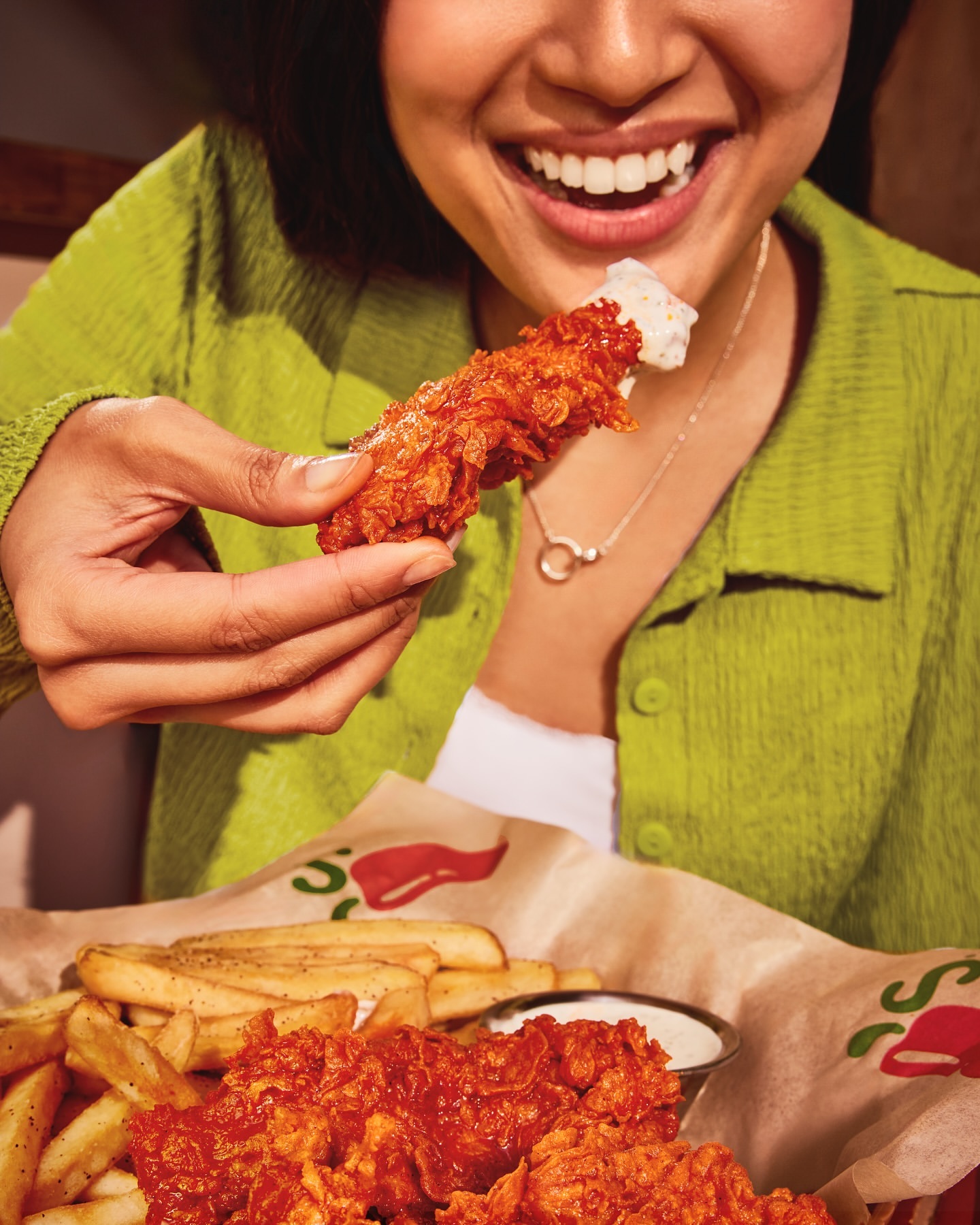 Woman enjoys a plate of chicken strips and fries at a restaurant. The focus is on the crispy chicken and casual dining atmosphere.