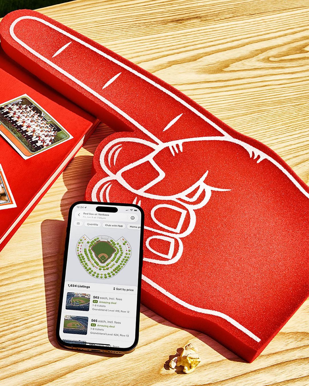 Overhead shot of an iPhone displaying a stadium seating chart next to a foam hand and a book on a wooden table.
