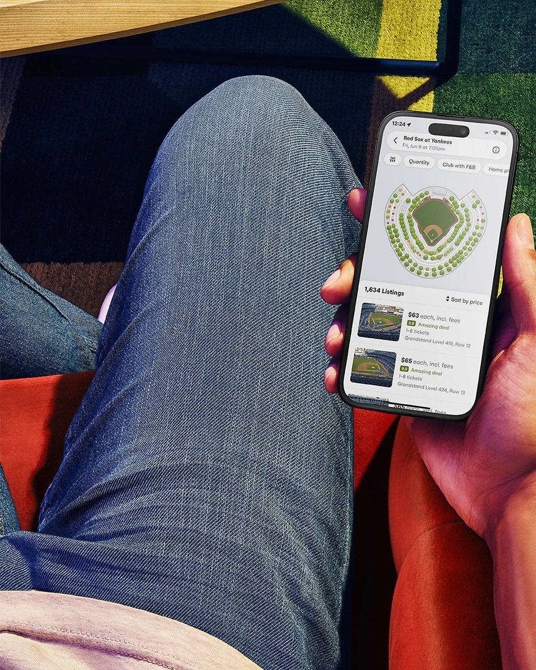 Person holding a smartphone displaying a stadium seating chart application, knees and legs visible in the frame.